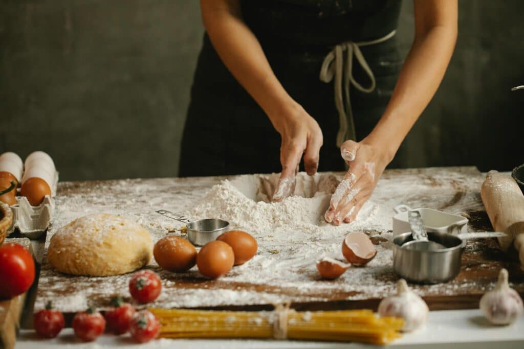 Hands preparing dough with fresh ingredients in a rustic kitchen setting.