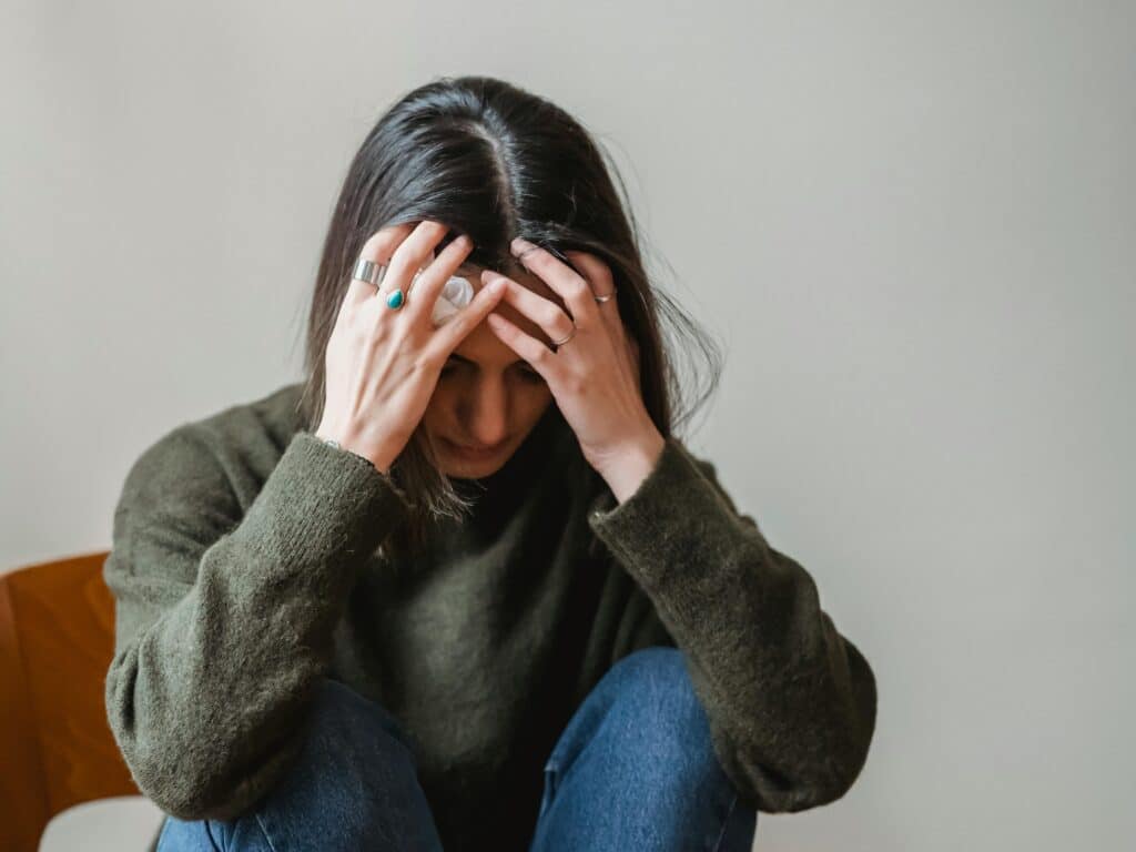 Young woman sitting on a chair indoors, appearing upset and thoughtful.