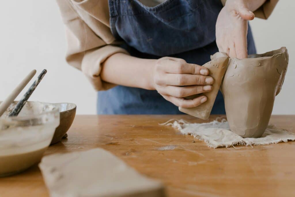 Close-up of hands shaping clay at a pottery worktable, showcasing the artistry of ceramics.