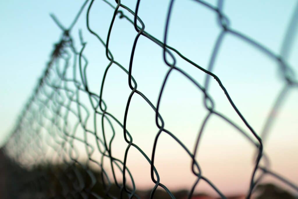 Detailed view of a chain-link fence against a soft, pastel sky background.
