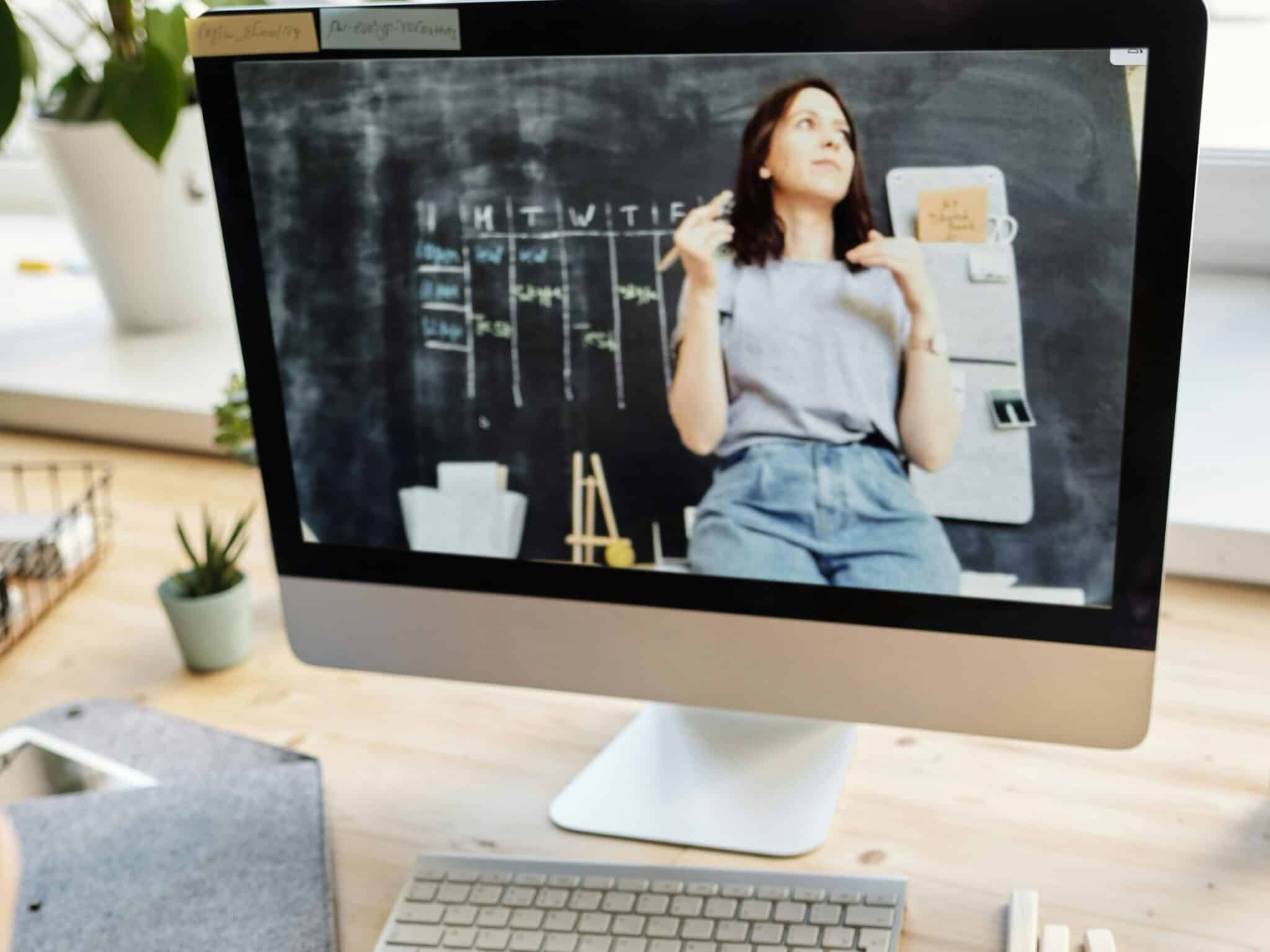 Student attending virtual class on a computer, taking notes at home.