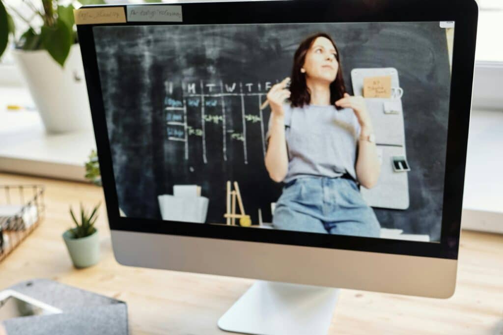 Student attending virtual class on a computer, taking notes at home.