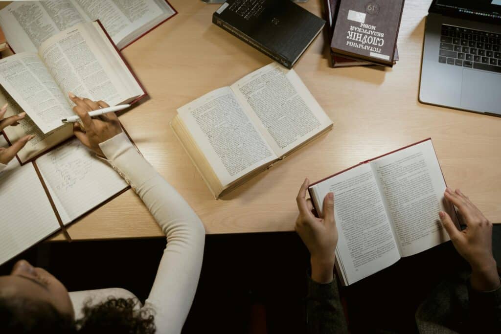 Group of adults studying together with open books and laptops on a wooden table.