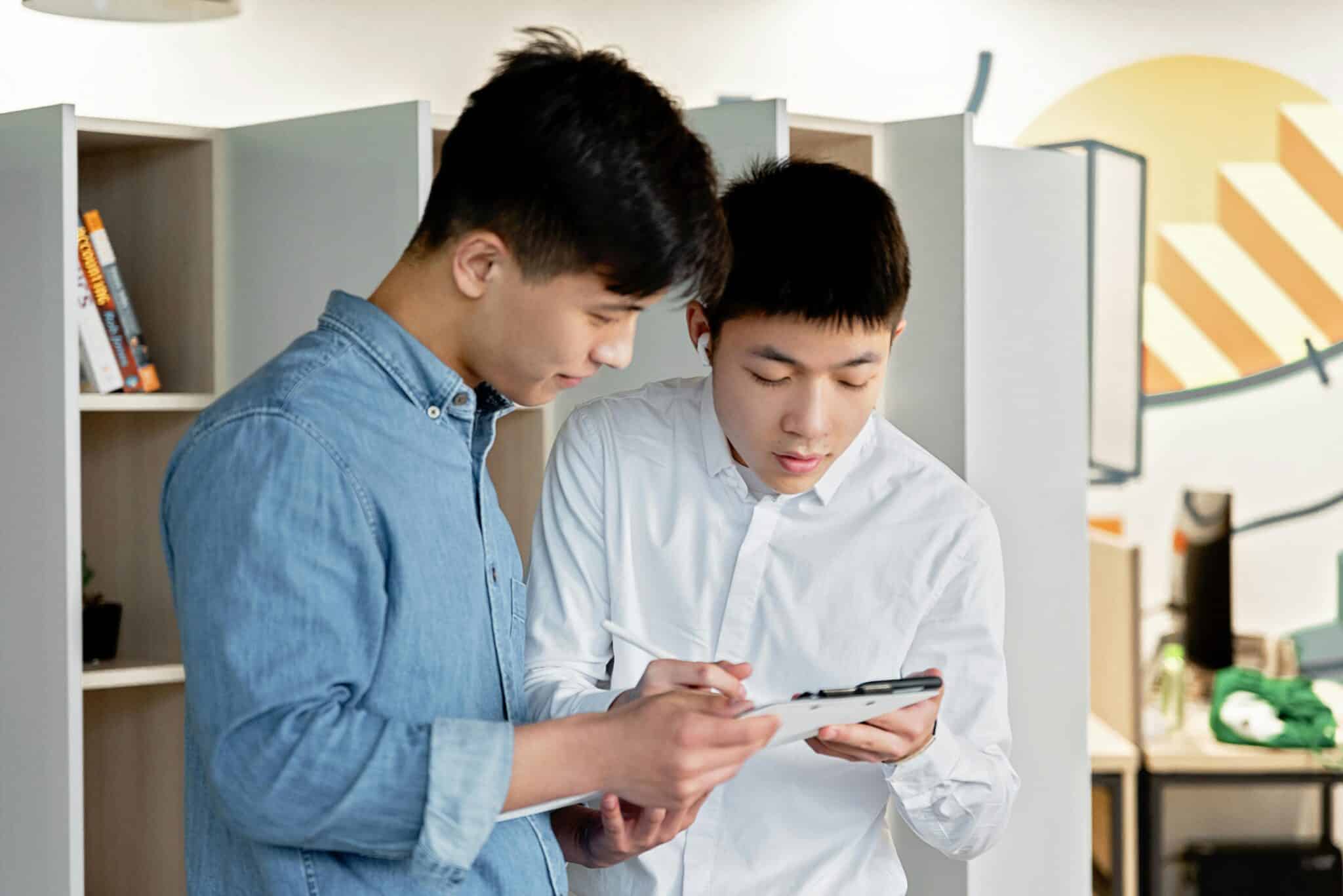 Two young men collaborating on a project using a digital tablet in a modern office environment.