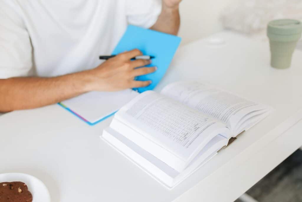 A close-up of an adult studying at a desk with an open book and notebook, capturing a moment of learning.