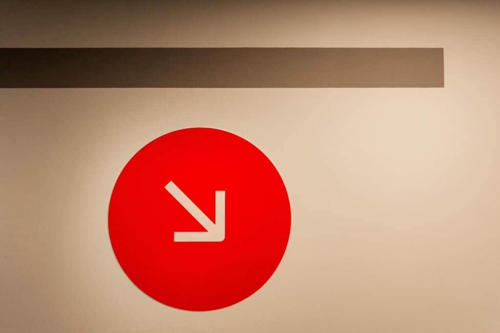 Red circle with white arrow on a minimalist wall, symbolizing direction and design.