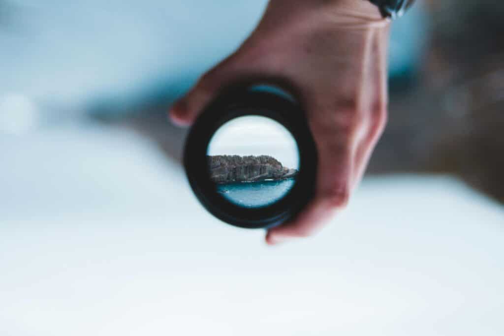 Crop anonymous male holding modern photo camera lens in hand against picturesque rough sea cliffs